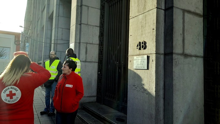 Røde Kors medarbejdere og to vagter står ved indgangen til Palais des Droits i Bruxelles.